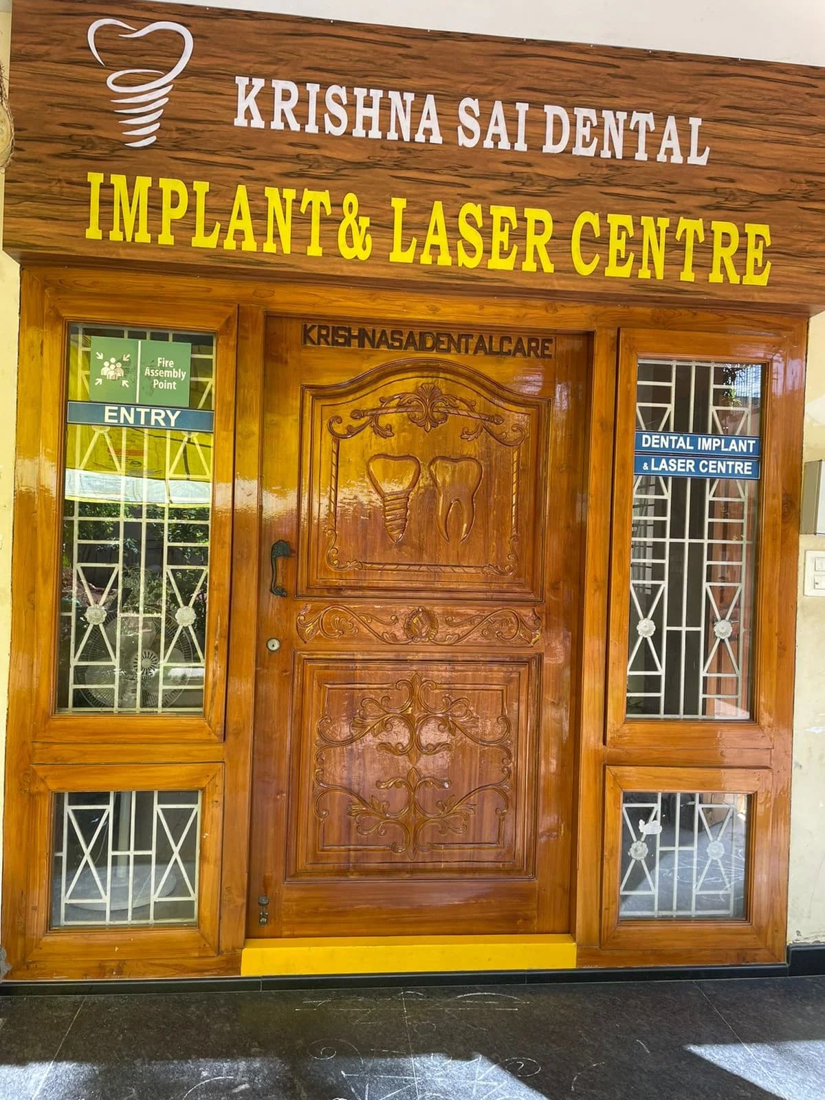 Krishna Sai EHS Dental Prasadampadu entrance with carved teakwood door and implant clinic signage